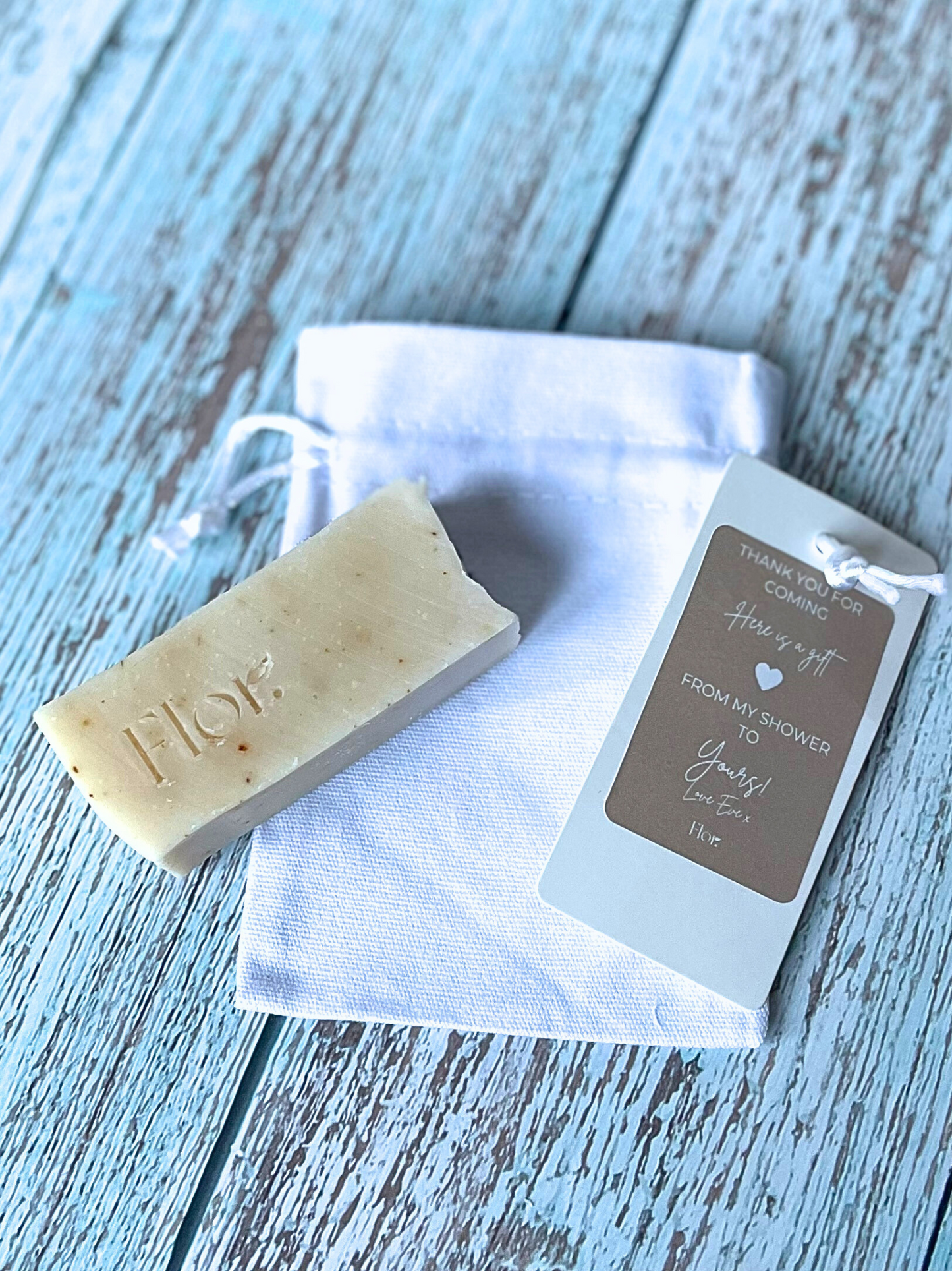 Half bar wedding event natural soap favour scented with ylang ylang lavender and lemongrass. Included in the image is a white luxury cotton bag with silk drawstrings that the soap favour sits in. Neutral branding for a baby shower gift. Can be used for wedding favours, corporate gifting and corporate events
