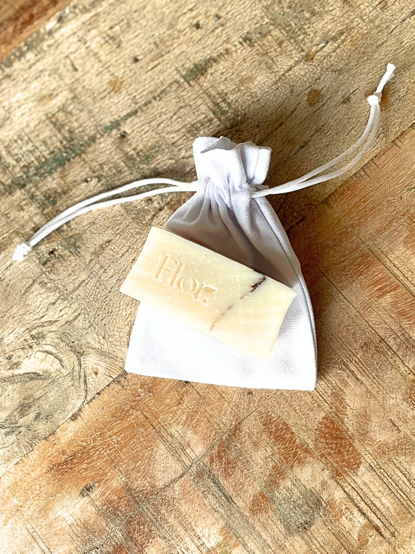 Min natural soap bar favour which is unscented and it decorated with a cocoa powder line through it.  The image also includes a luxury white cotton bag with silk drawstrings that the soap favour comes in. Can be used with weddings baby showers corporate gifting and corporate events