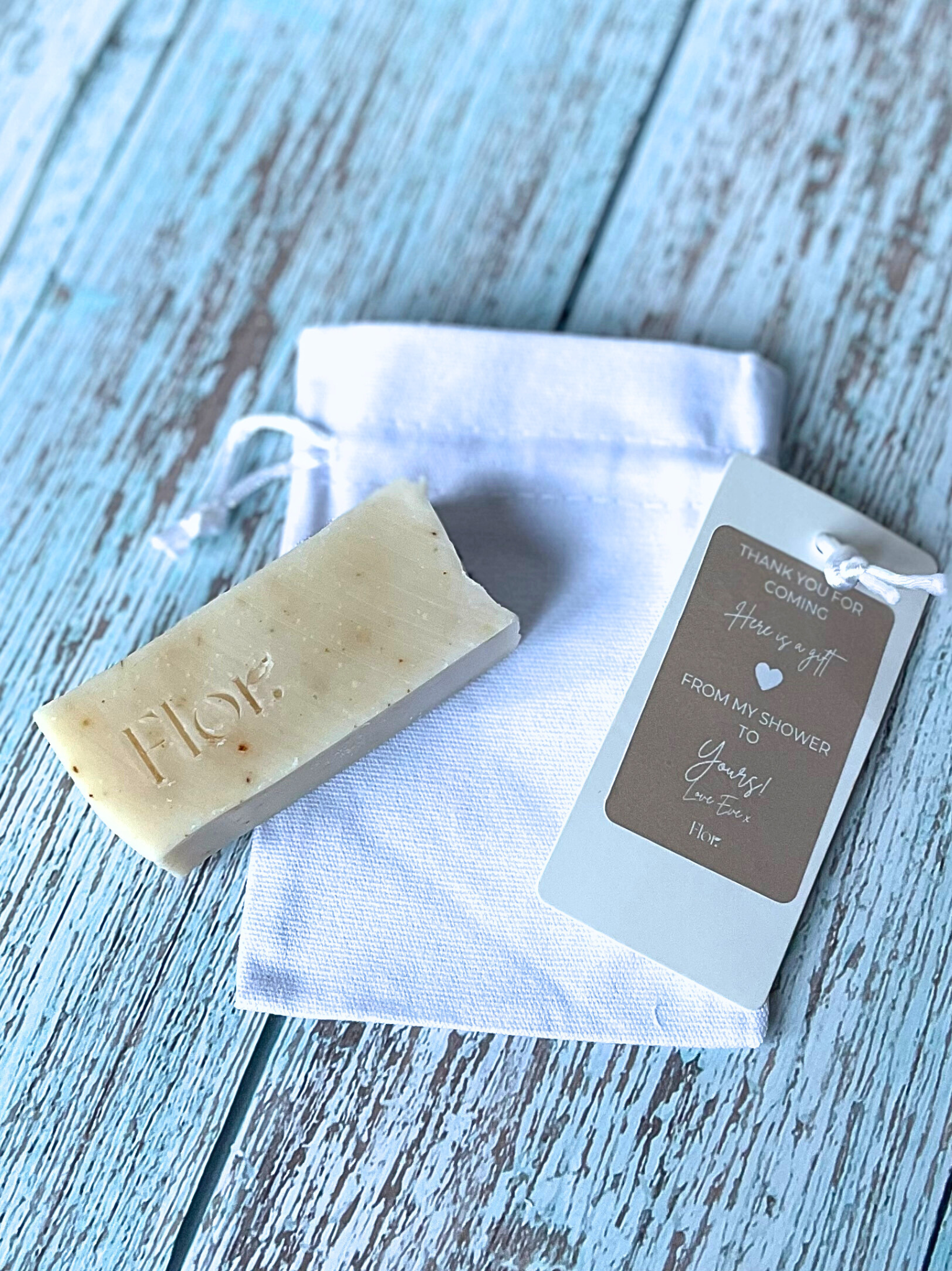 Half bar wedding event natural soap favour scented with ylang ylang lavender and lemongrass.  Included in the image is a white luxury cotton bag with silk drawstrings that the soap favour sits in. Neutral branding for a baby shower gift. Can be used for wedding favours, corporate gifting and corporate events
